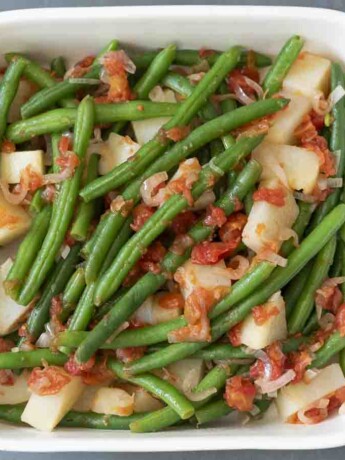 An overhead view of a pan of green beans with potato and tomato