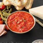 Roasted red pepper relish in a bowl with crusty bread, pickles and cherry tomatoes