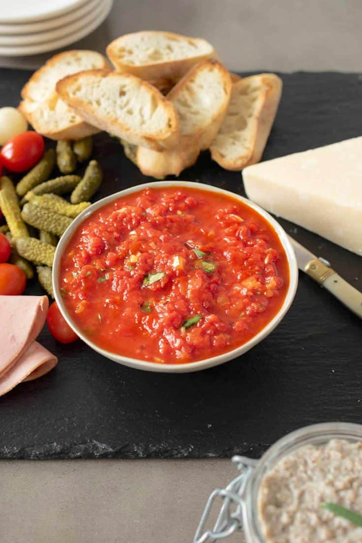 Roasted red pepper relish in a bowl with crusty bread, pickles and cherry tomatoes