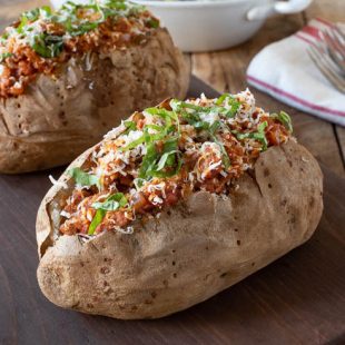 2 Italian sausage microwave baked potatoes on a serving board with forks in the background