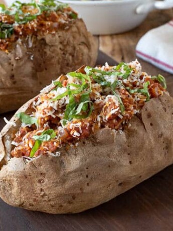 2 Italian sausage microwave baked potatoes on a serving board with forks in the background