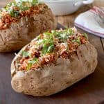 2 baked potatoes filled with Italian sausage and tomato sauce topped with fresh basil
