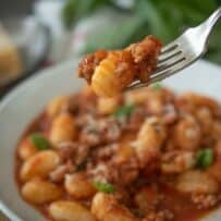A piece of gnocchi on a fork with meat sauce