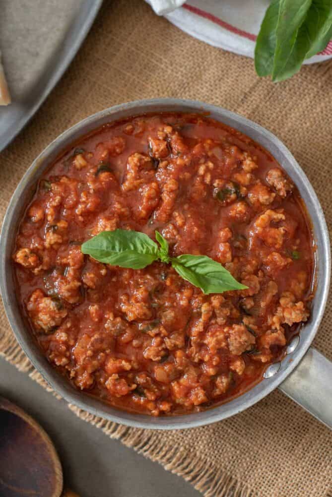 A pan of sausage tomato sauce garnished with basil
