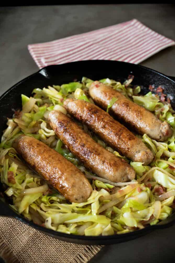 A cast iron skillet of cabbage cooked with pancetta, topped with sausages