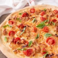 A closeup of the pizza showing the Italian sausage crumbles, caramelized onions, cherry tomatoes and fresh basil