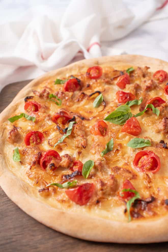 A closeup of the pizza showing the Italian sausage crumbles, caramelized onions, cherry tomatoes and fresh basil