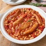 A round serving plate of Italian sausage and beans in a tomato sauce