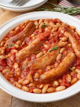 A round serving plate of Italian sausage and beans in a tomato sauce