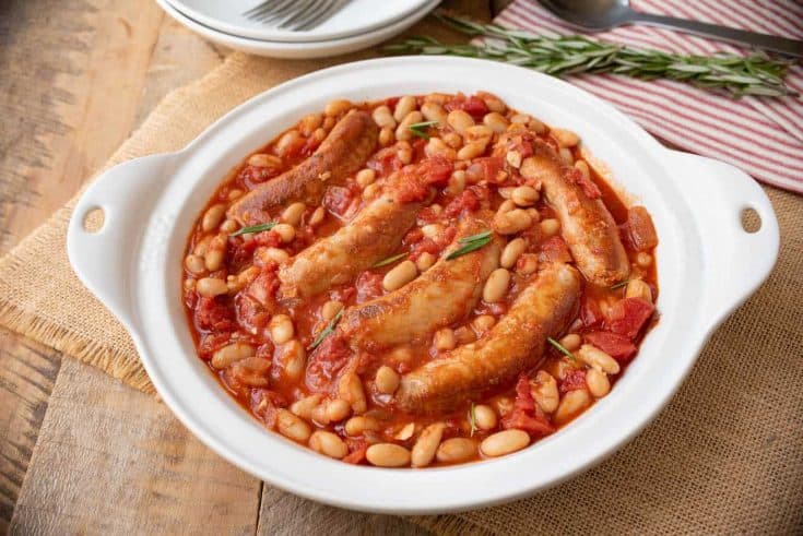 A round serving plate of Italian sausage and beans in a tomato sauce