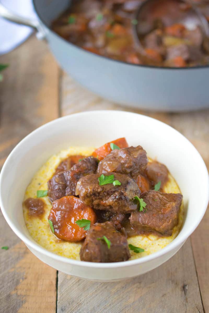 A closeup of a bowl of Italian beef stew on a bed of polenta in a white bowl