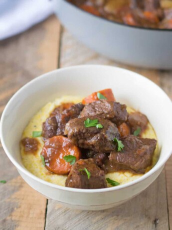 Italian beef stew served in a white bowl over creamy polenta