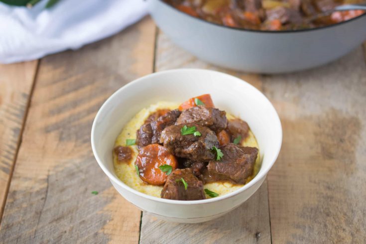 Italian beef stew served in a white bowl over creamy polenta