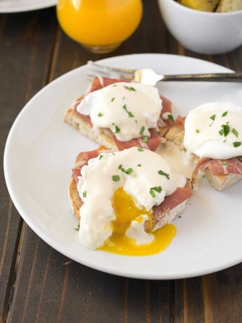 A poached egg on top of prosciutto and ciabatta bread cut open with yellow yolk running out