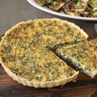 A spinach quiche on a round serving board with 1 cut piece
