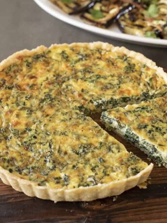 A spinach quiche on a round serving board with 1 cut piece