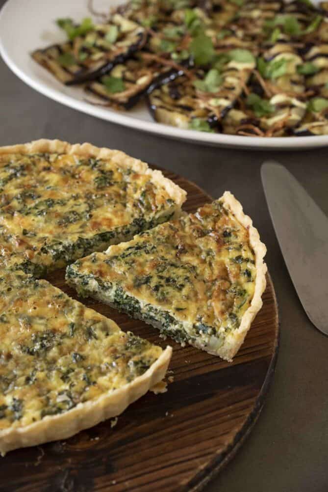 A quiche on a round cutting board with a slice separate