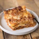 A slice of lasagna Bolognese on a white plate with a fork
