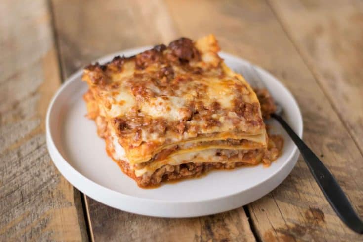A slice of lasagna Bolognese on a white plate with a fork