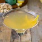 A closeup of a yellow cocktail with a twist of lemon rind