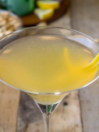 A closeup of a yellow cocktail with a twist of lemon rind