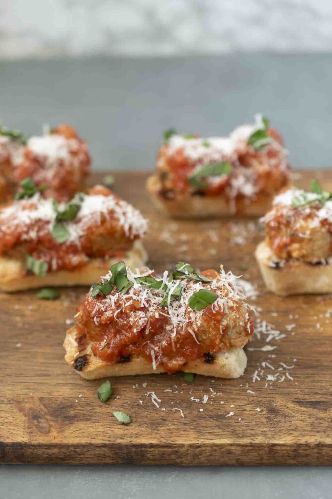 5 Meatball crostini on a serving board with grated Parmesan cheese