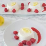 Lemon panna cotta on a white plate surrounded by raspberry sauce and fresh raspberries