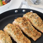 4 Lemon parmesan crusted salmon filets cooking in a large skillet