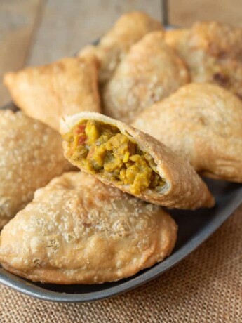 A cut open samosa showing the lentil curry filling laying on a plate with other samosa