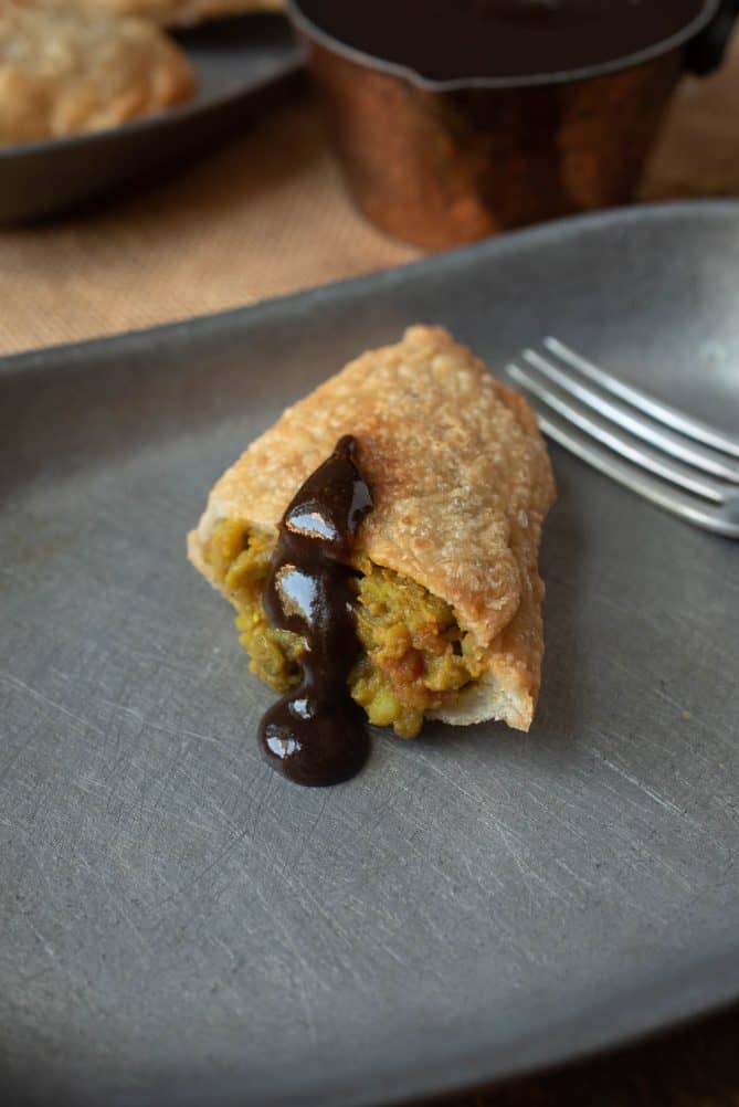 Half of a lentil samosa on a plate drizzled with tamarind chutney that is dark brown in color