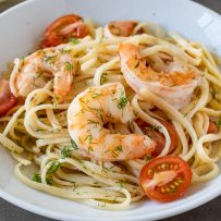 Meaty shrimp served over linguine with tomatoes and dill in a white bowl