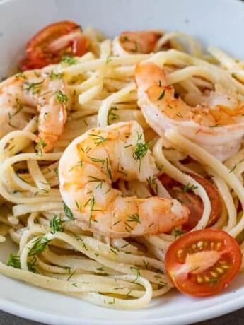 Meaty shrimp served over linguine with tomatoes and dill in a white bowl