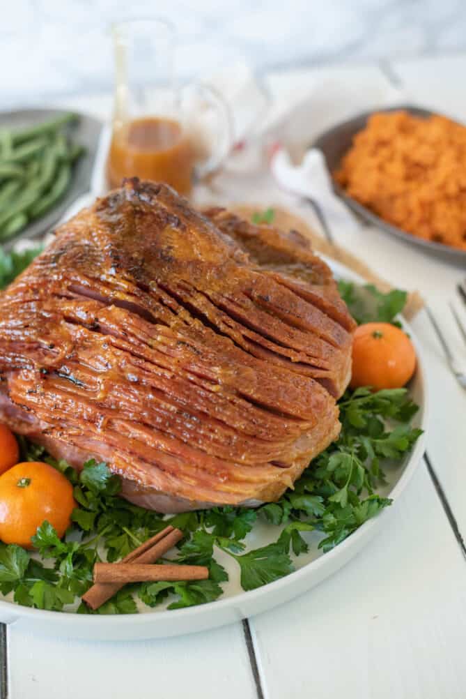 A perfectly glazed ham on a platter with green garnish and mandarin oranges