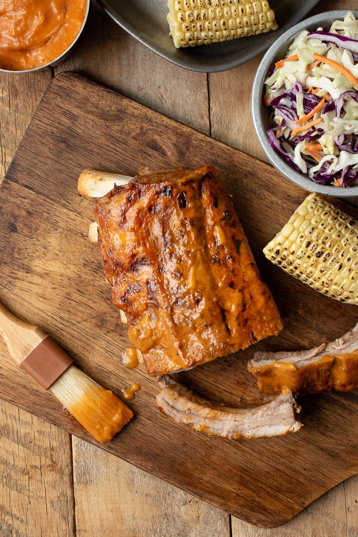 The ribs from above on a cutting board with coleslaw and corn on the cob