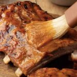 Brushing mango bbq sauce over grilled ribs