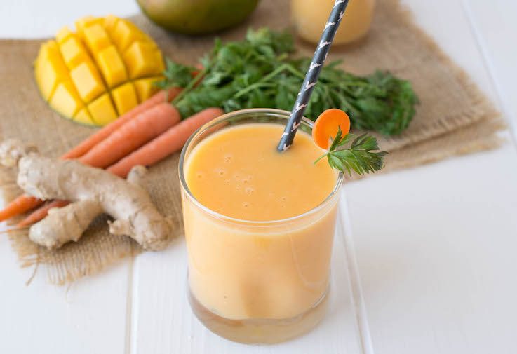 Smoothie in a short glass with a straw with fresh ginger, carrots and mango
