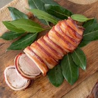 Maple bacon wrapped pork tenderloin on a bed of leaves on a cutting board