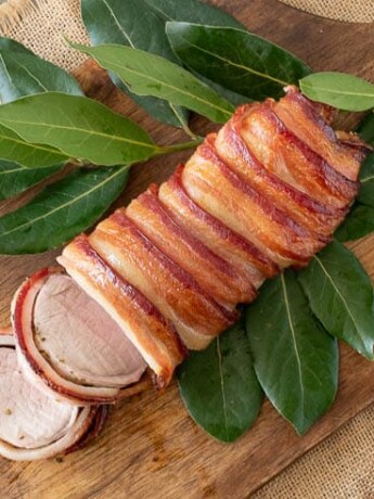 Maple bacon wrapped pork tenderloin on a bed of leaves on a cutting board