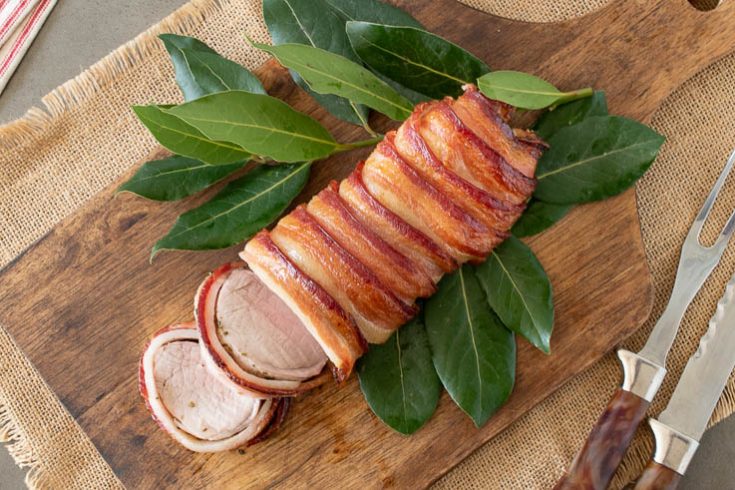 Maple bacon wrapped pork tenderloin on a bed of leaves on a cutting board