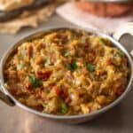 A round copper bowl with handles filled with mashed Indian eggplant and cilantro