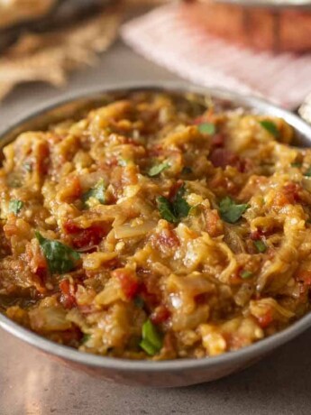 A round copper bowl with handles filled with mashed Indian eggplant and cilantro