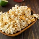 A rectangle bowl of Mexican popcorn with lime wedges