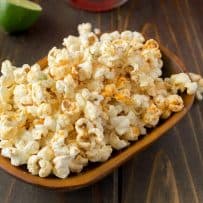 A rectangle bowl of Mexican popcorn with lime wedges