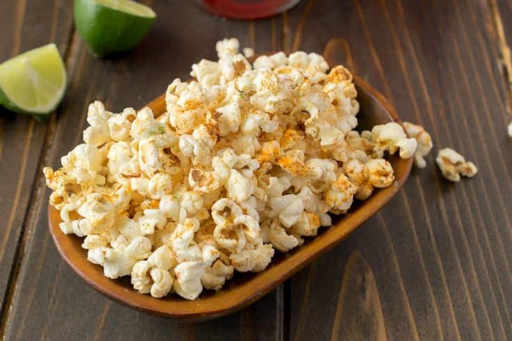 A rectangle bowl of Mexican popcorn with lime wedges