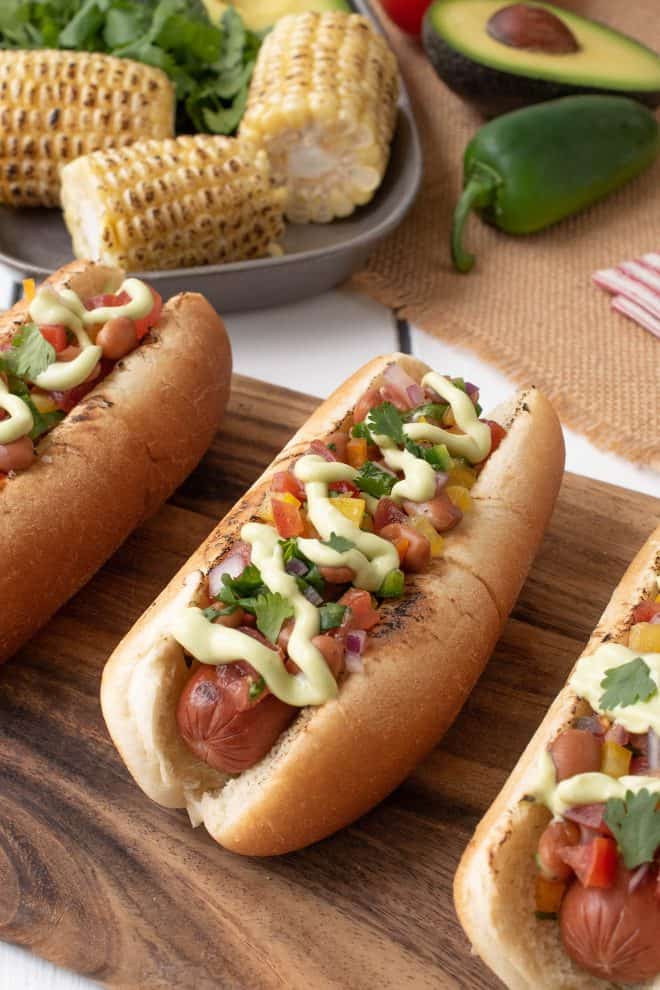 Mexican hot dogs on a serving board served with corn on the cob