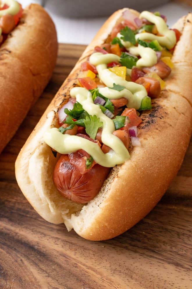 Hot dog and bun with fresh toppings of salsa, avocado cream and cilantro
