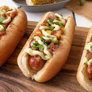 3 Mexican Style Hot Dogs lined up on a board