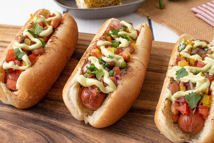3 Mexican Style Hot Dogs lined up on a board