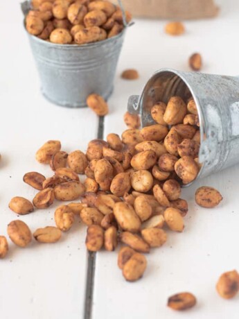 A small silver bucket filled with peanuts that has fallen over