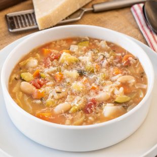 A white bowl filled with minestrone soup with beans and vegetables